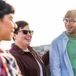 Three young people talking together and laughing outdoors in the sunlight